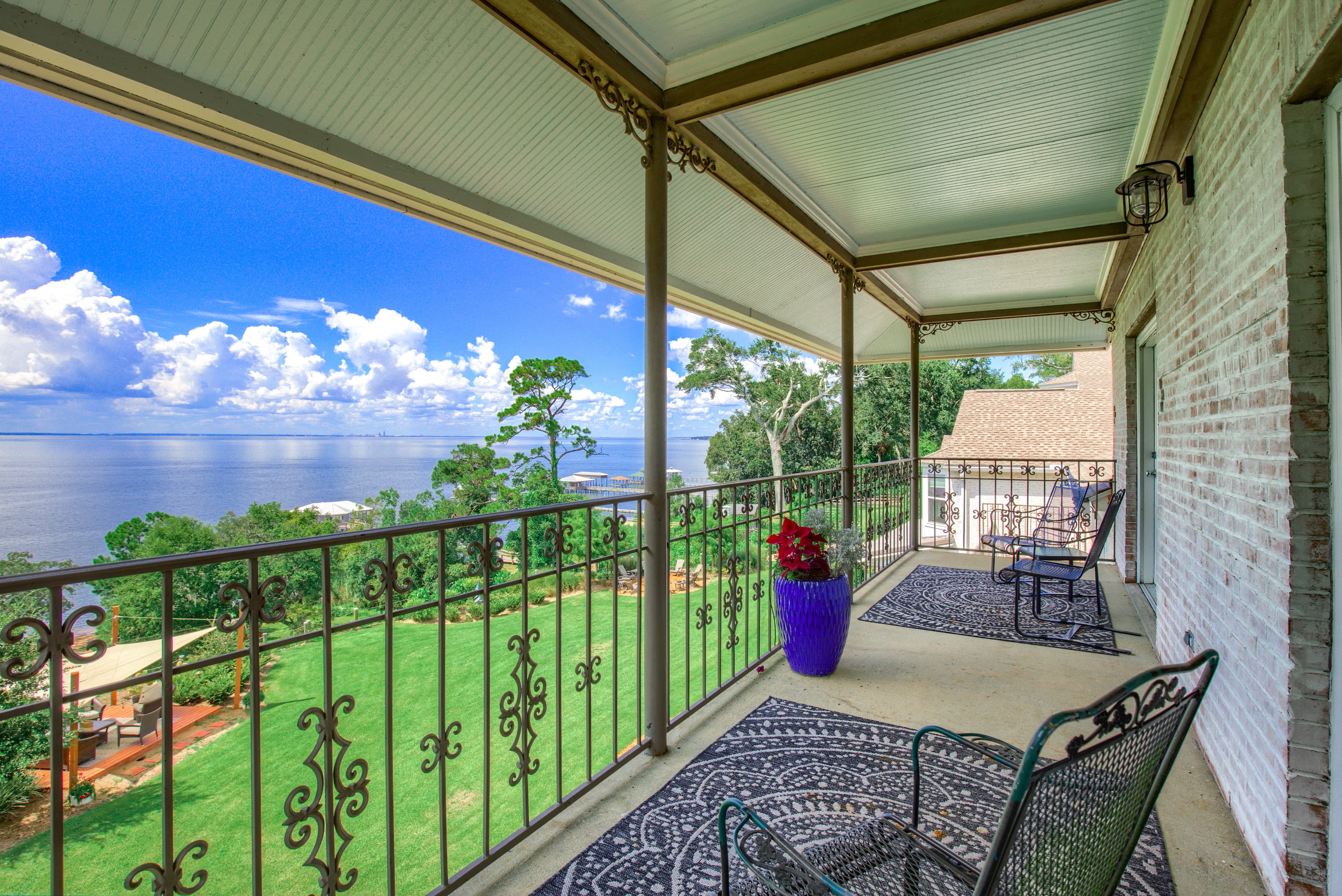 Porch Area with iron railing and chairs overlooking Mobile Bay, lush green grounds and bright blue sky