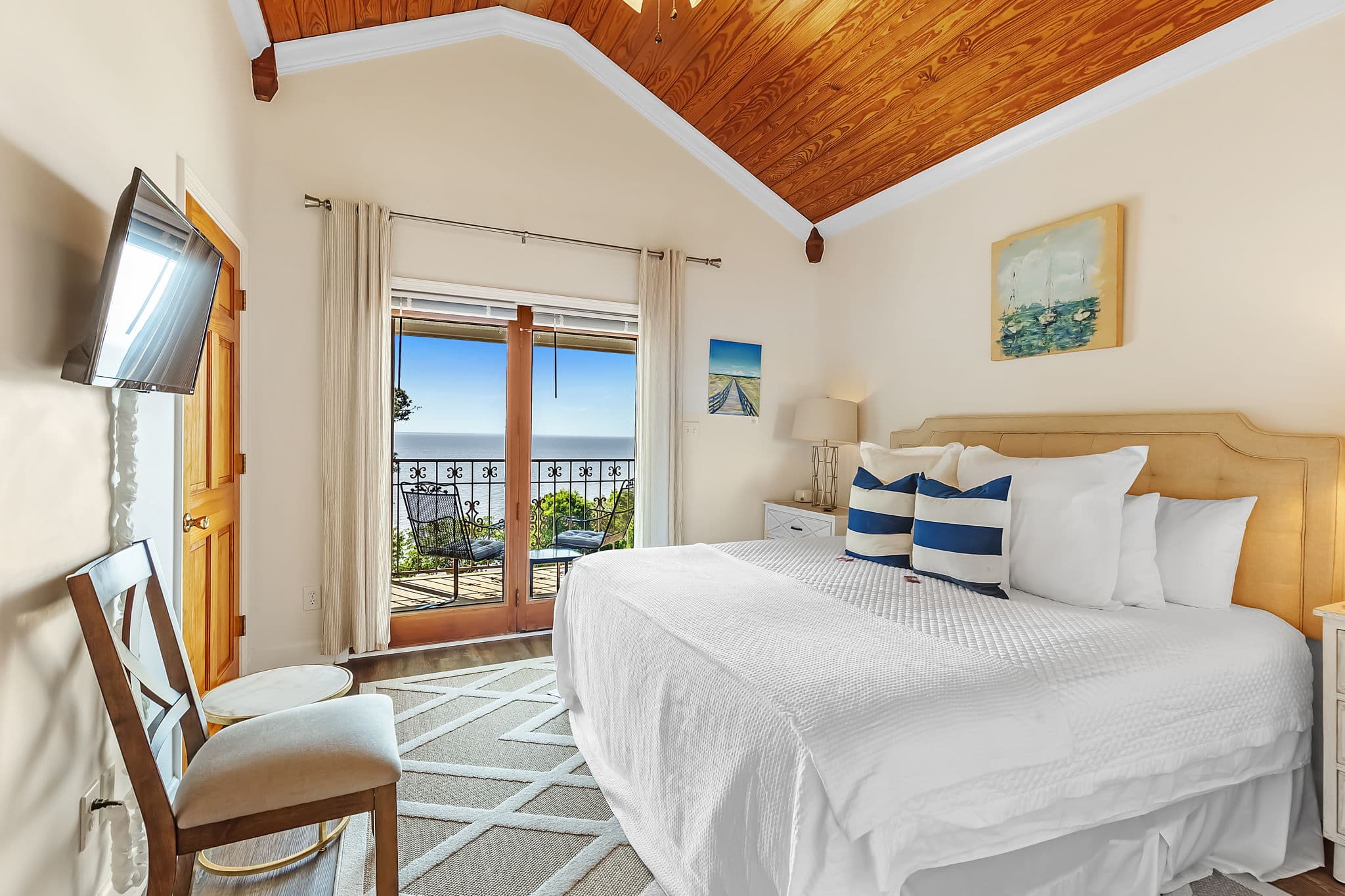 Bay View Bedroom with king bed topped with pristine white bedding and pillows, flat-screen wall-mounted TV opposite, and sliding doors leading to bay view balcony