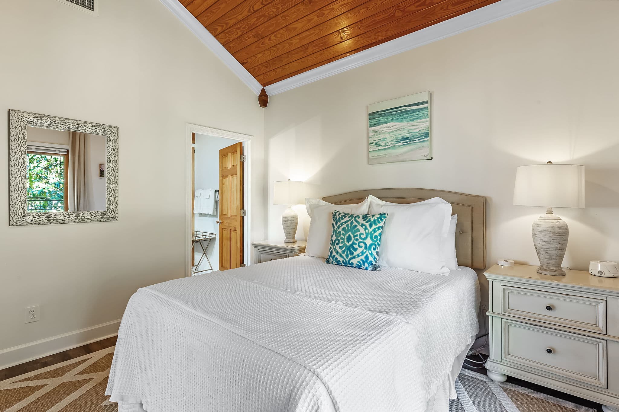 Second Bedroom with king bed with white bedding and throw pillows flanked by matching wooden nightstands and table lamps, with door leading to attached bathroom