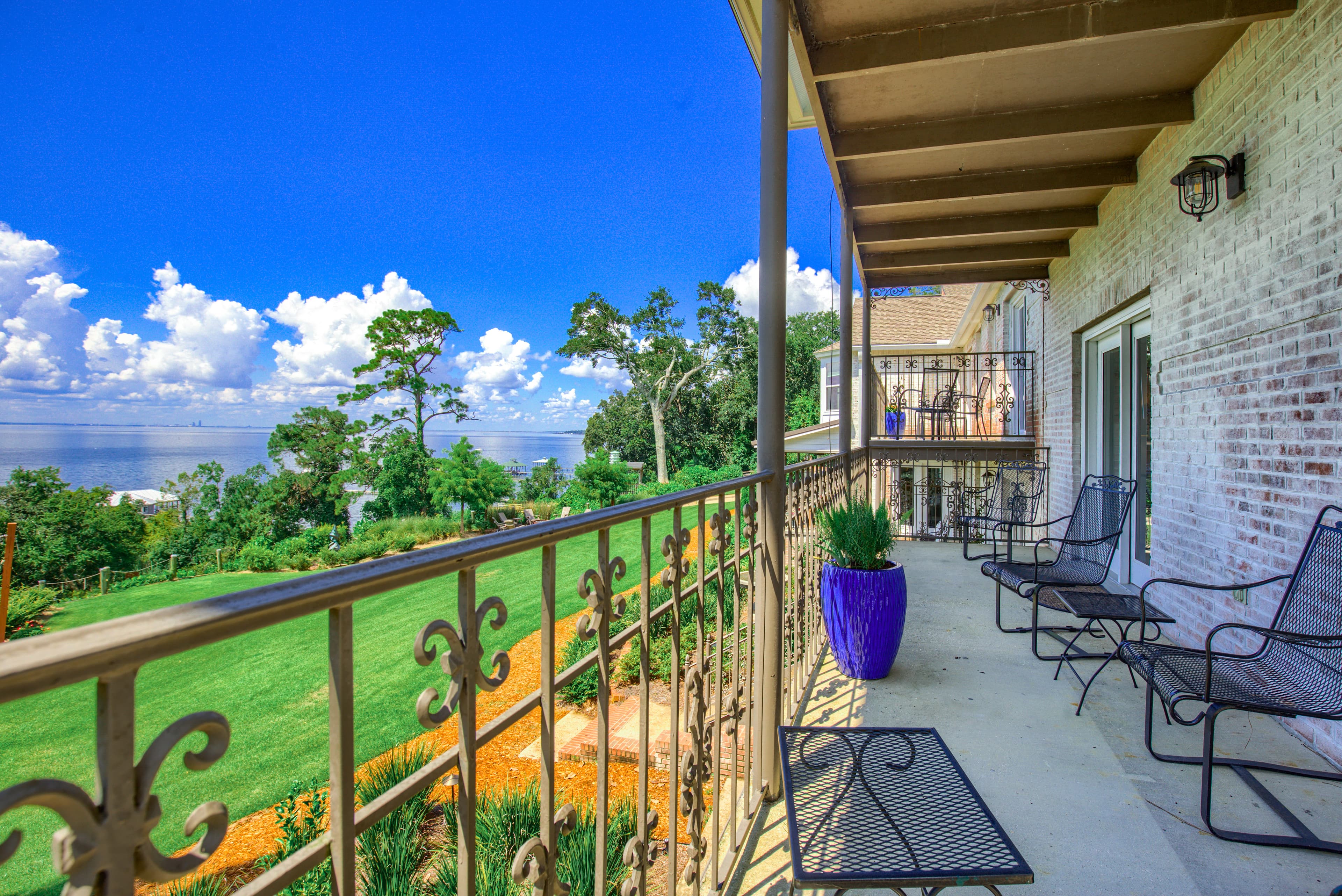 Porch with decorative metal railing overlooking bay and furnished with metal chairs
