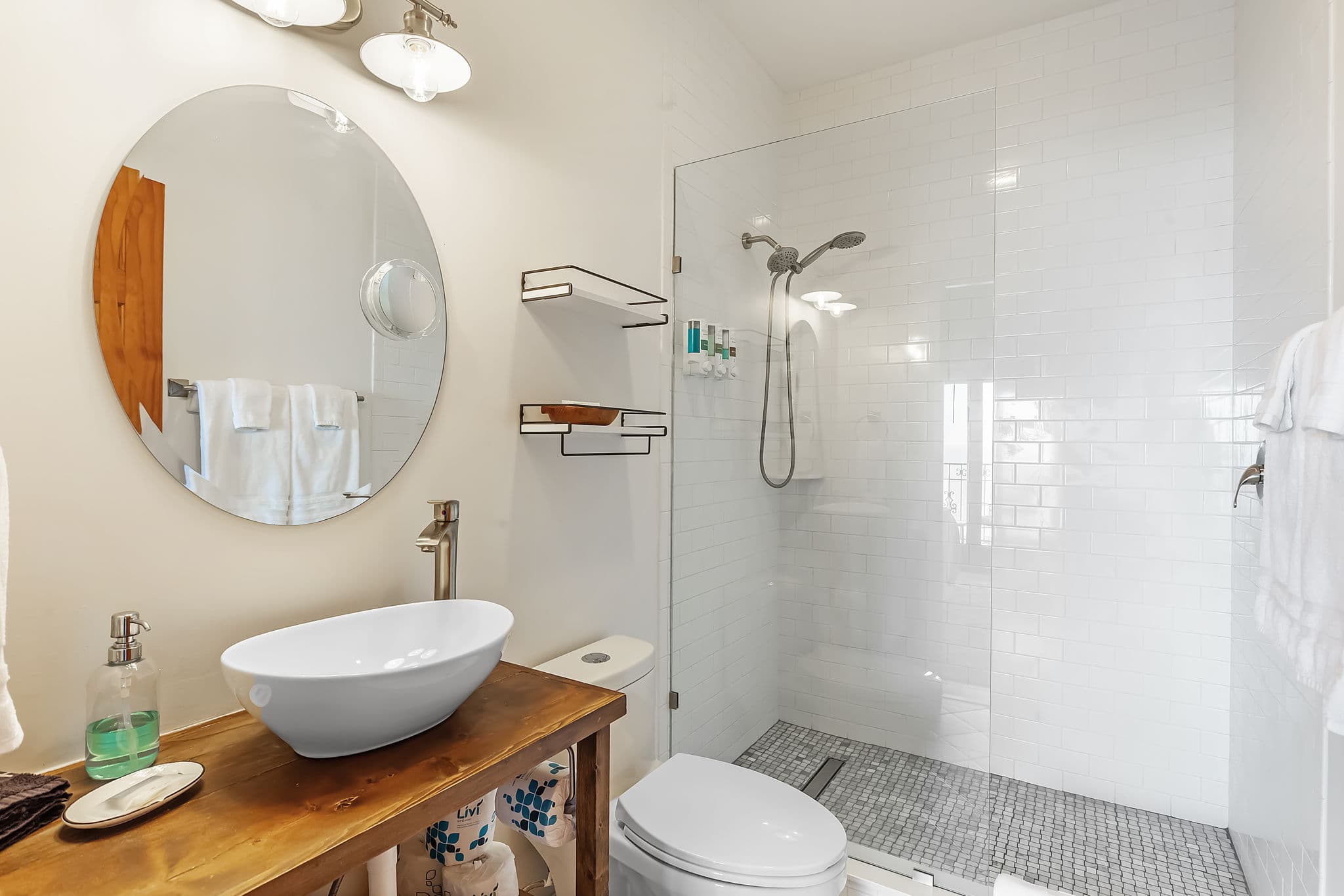 Bright white bathroom with walk-in tiled shower, toilet, and wooden vanity with vessel sink