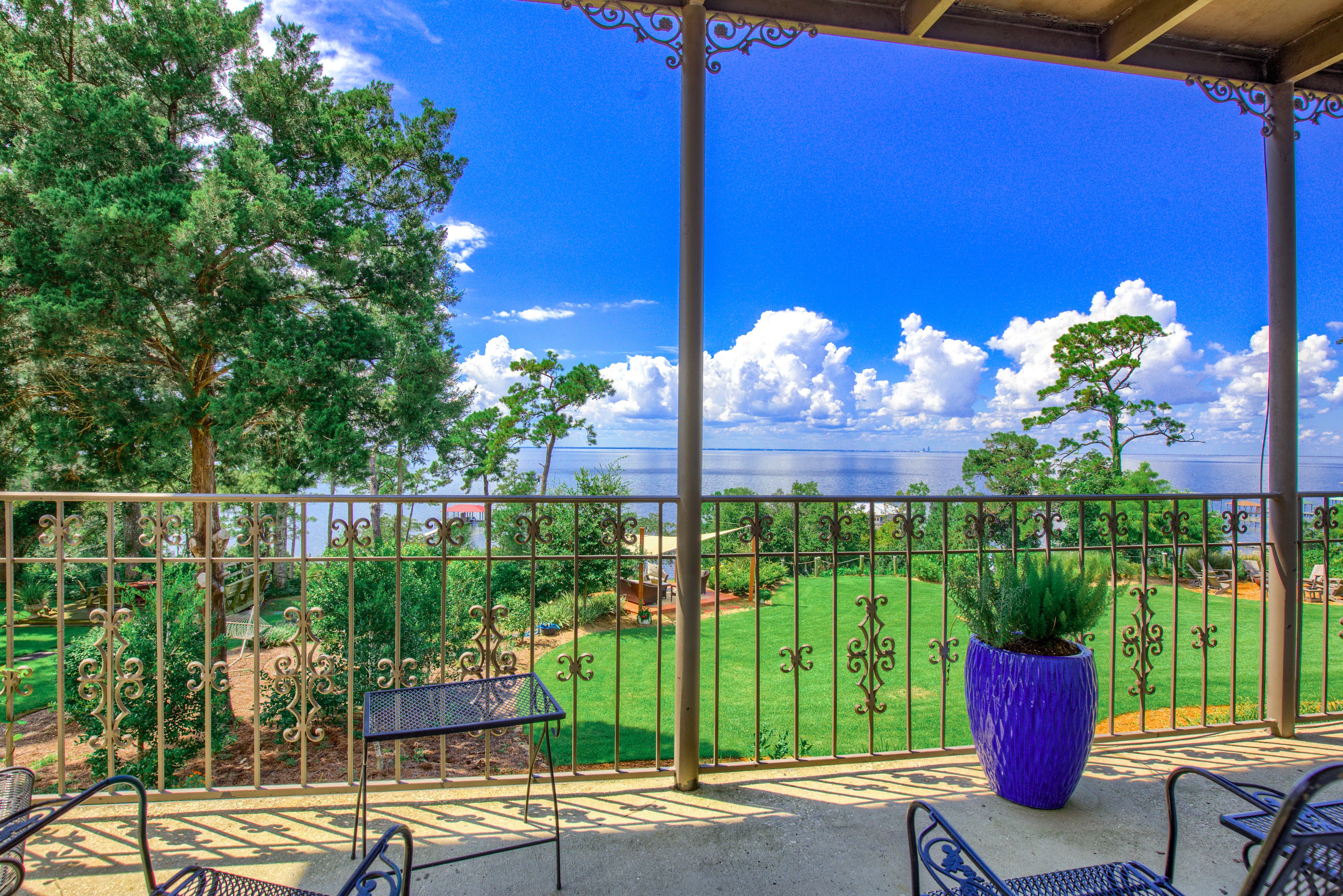 Balcony with iron railing and chairs overlooking the beautifully manicured lawn and bright blue sky over the bay