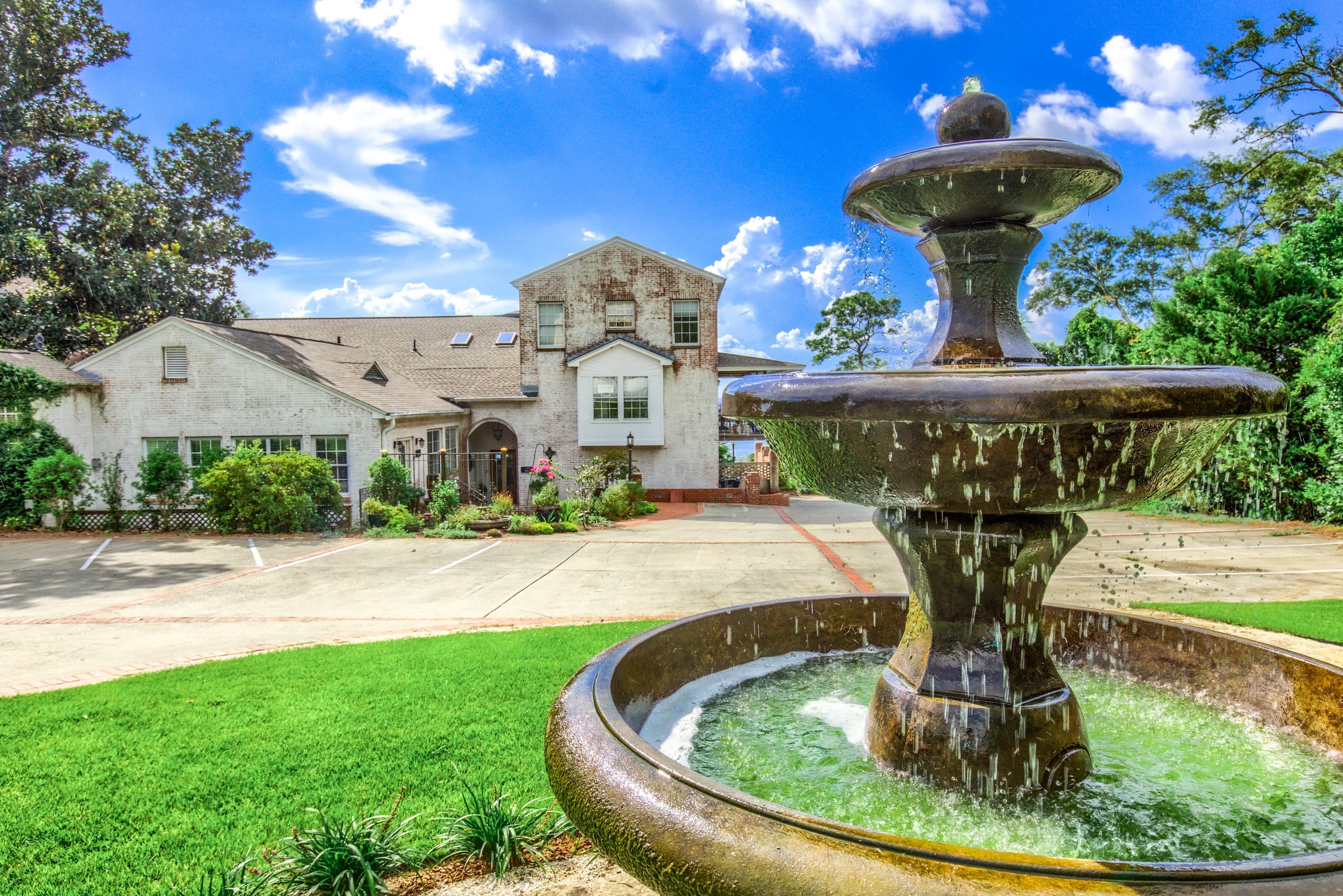 A large, luxurious house with a fountain in the foreground. The house has a white  exterior and a large driveway.