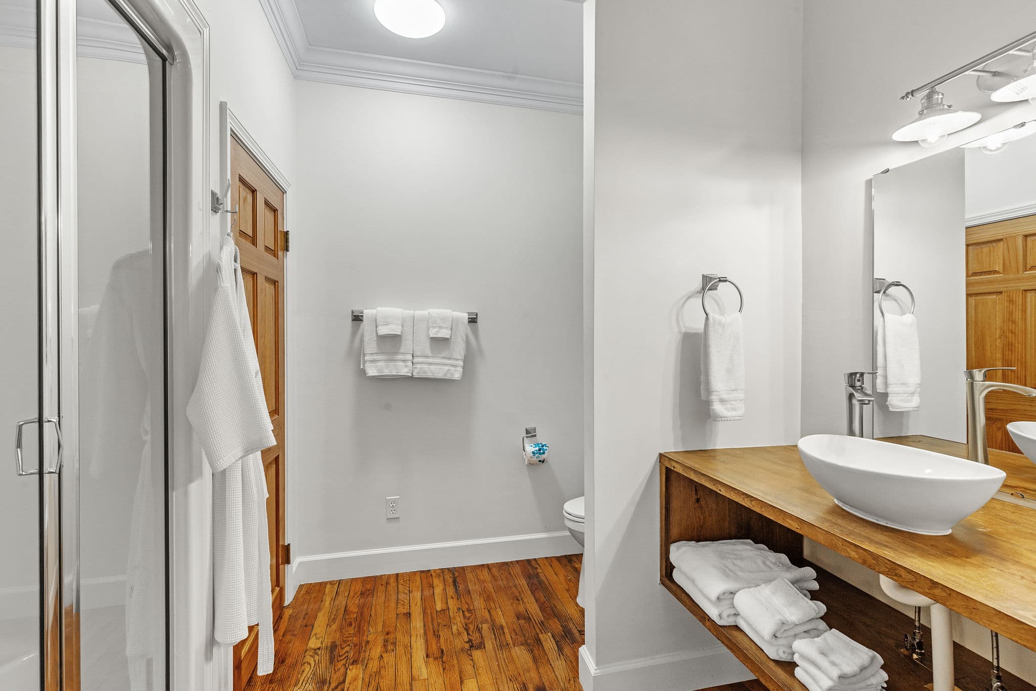 Attached private bathroom with a white sink and vanity, a toilet, and a shower. The bathroom has hardwood floors and a mirror on the wall.
