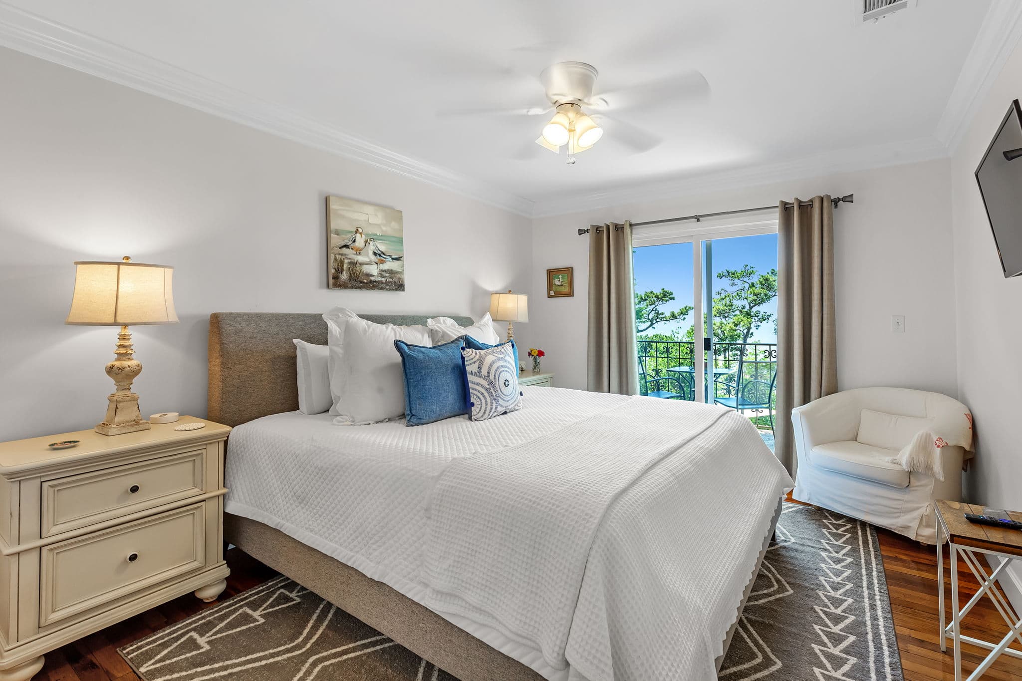 Bay View Bedroom with king bed flanked by nightstands with table lamps, a cozy barrel chair in the corner, and sliding doors leading to a balcony with bay views