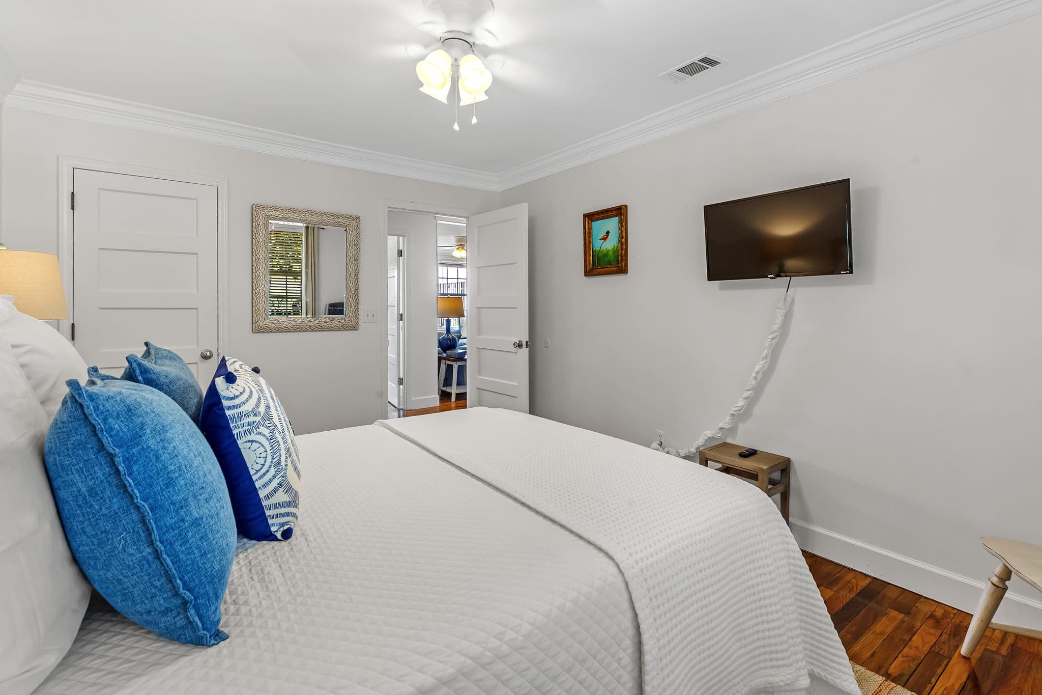 Second Bedroom - View across queen bed topped with plump pillows shows flat-screen TV mounted on opposite wall and door leading to living area