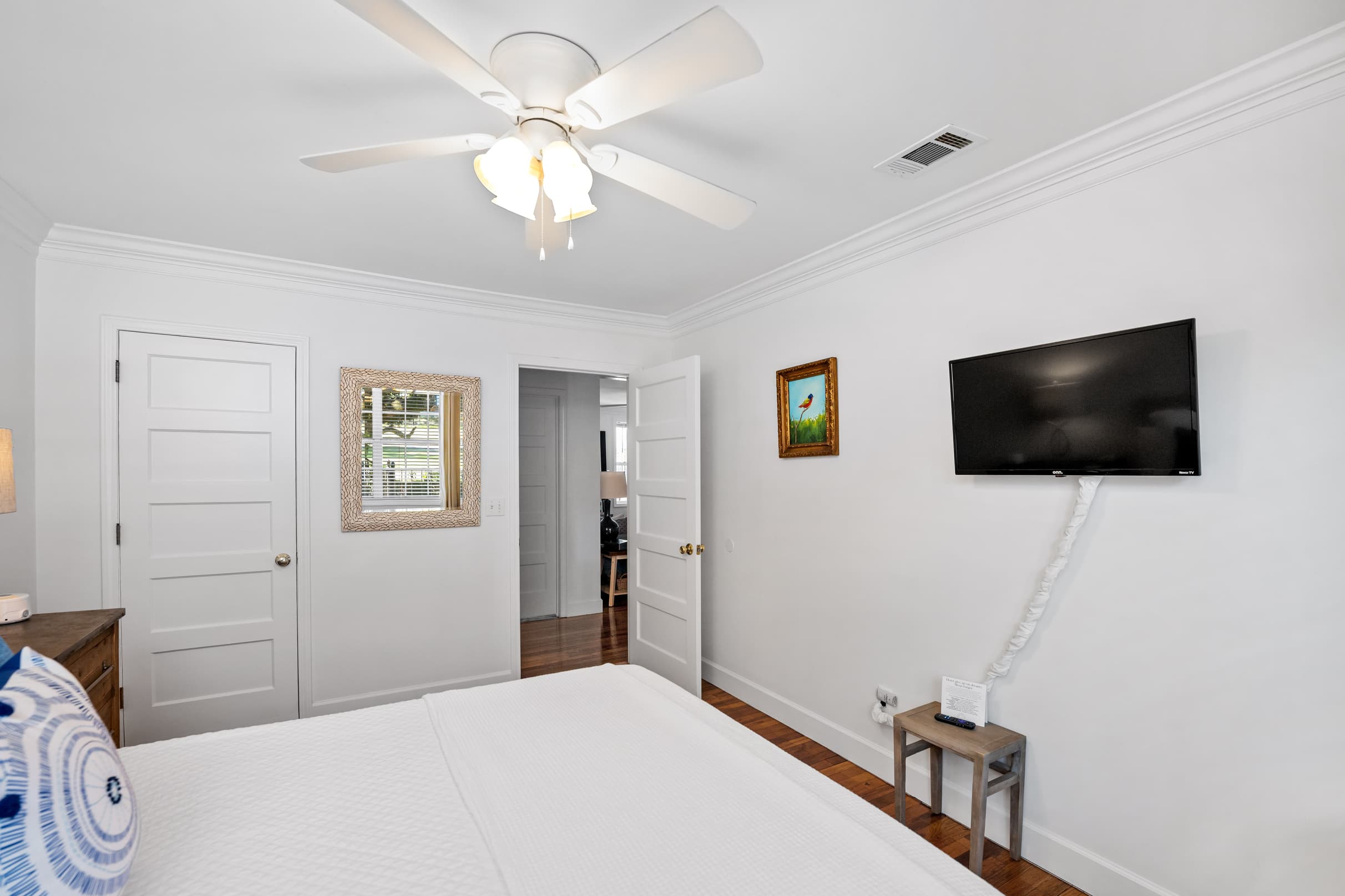 Second Bedroom - View across queen bed topped with plump pillows shows flat-screen TV mounted on opposite wall and door leading to living area