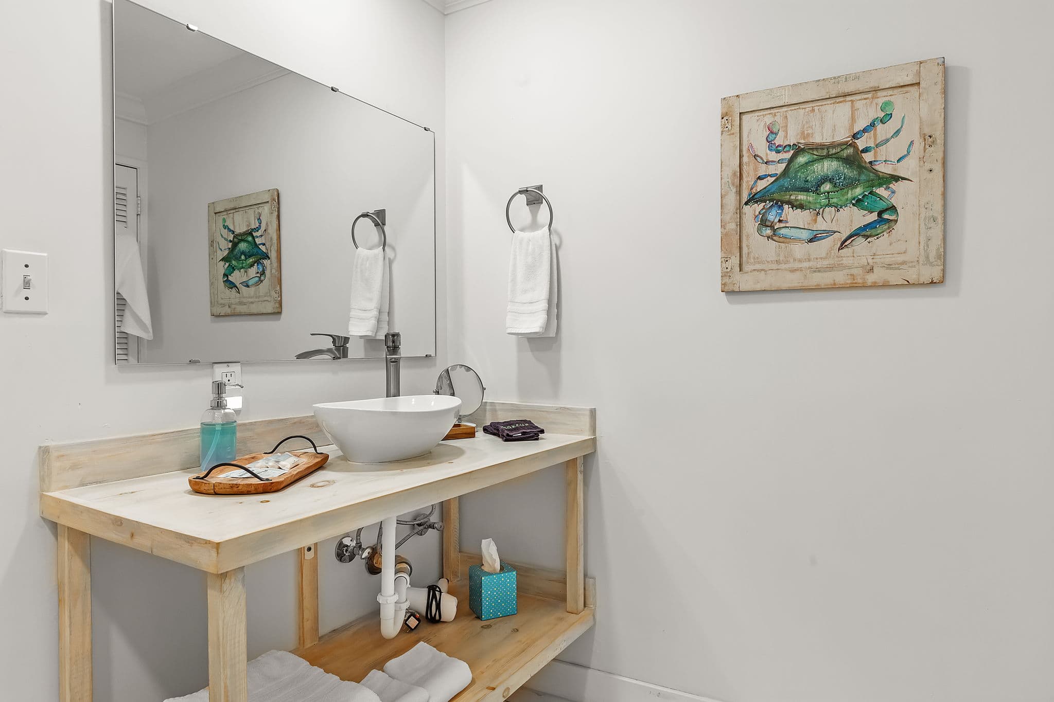 Pristine white bathroom with natural wood vanity featuring vessel sink and art work with blue & green crab on wall