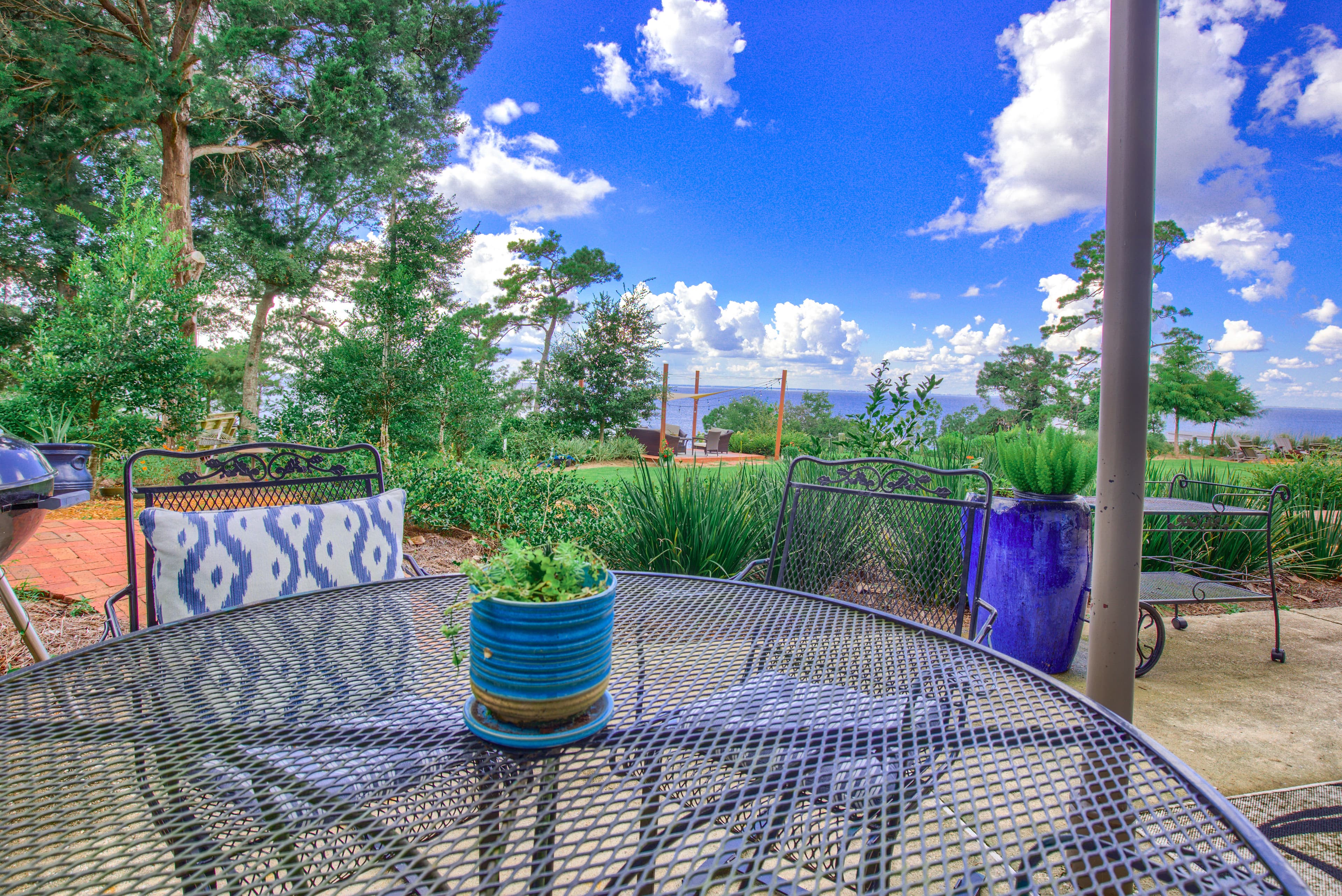 A patio with a round metal table and chairs with bay views. There are potted plants on the table and on the patio.
