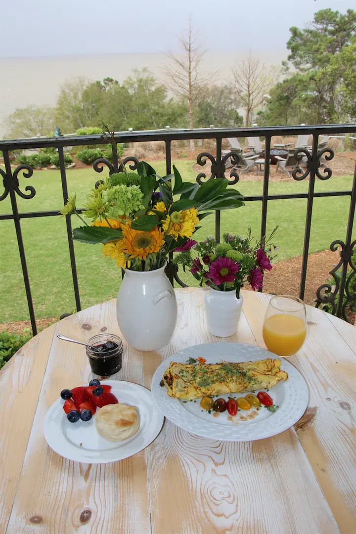 A delicious breakfast spread on our Bay View porch. The table is set with a plate of an omelet with vegetables, a plate of fruit, a glass of orange juice, and a vase of fresh flowers.