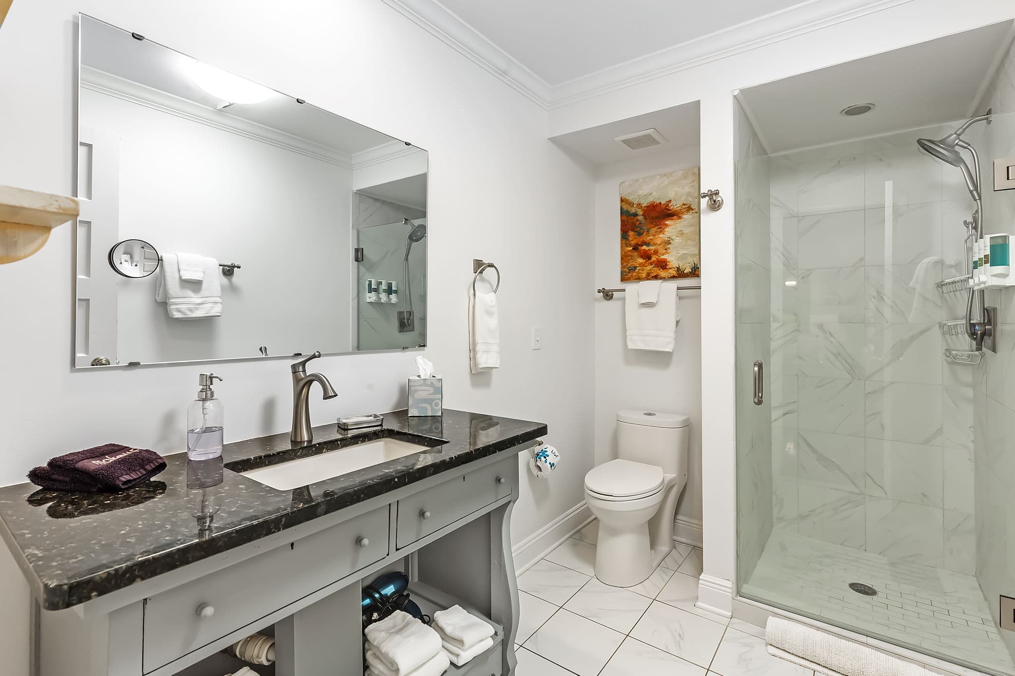 A clean and spacious bathroom with a large walk-in shower, a toilet, and a vanity with a sink and mirror. The bathroom has tiled floors and a modern design.