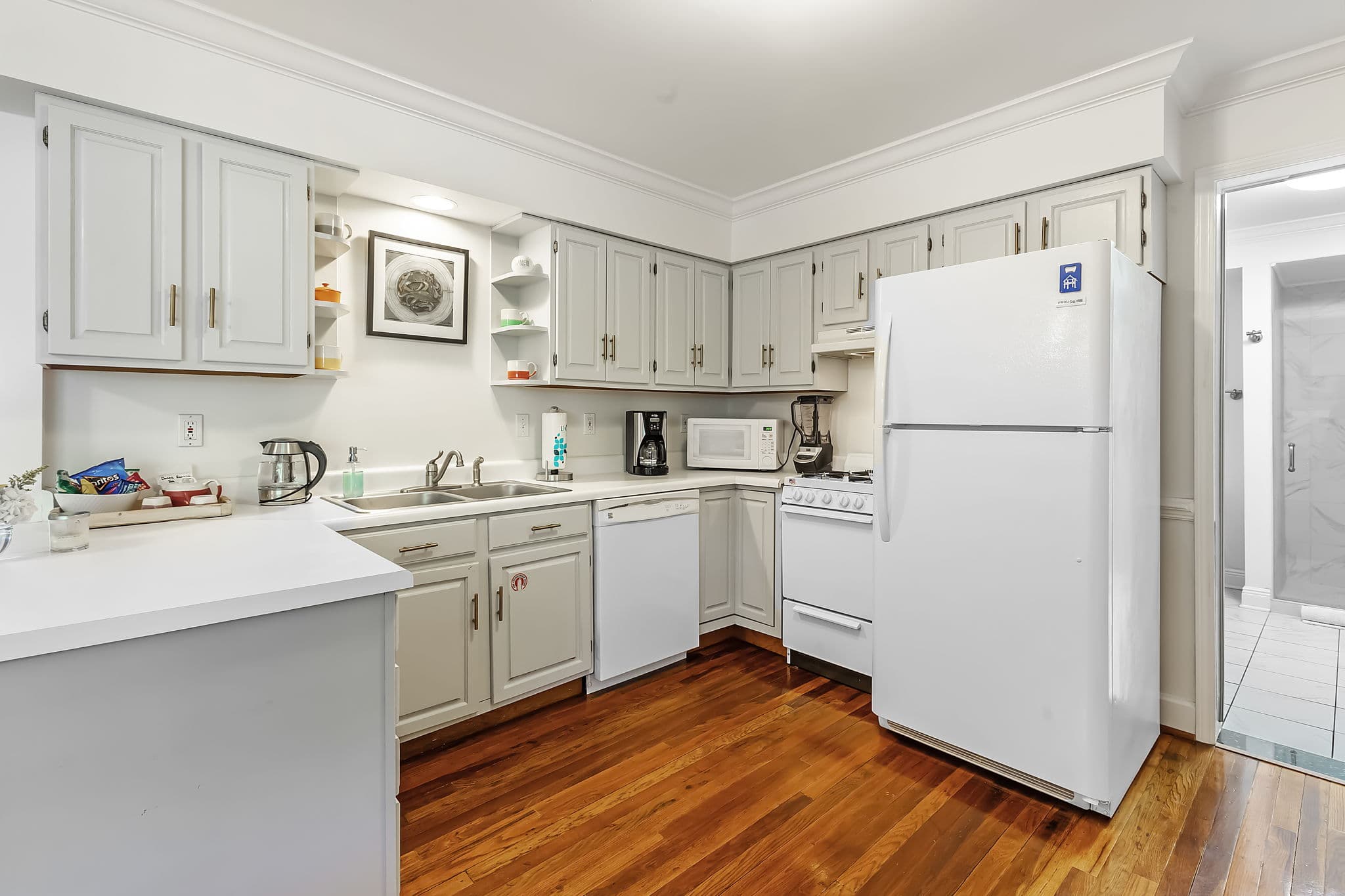 A well-equipped kitchen with white cabinets and appliances. The countertops are a warm wood tone, and there's a beautiful hardwood floor.