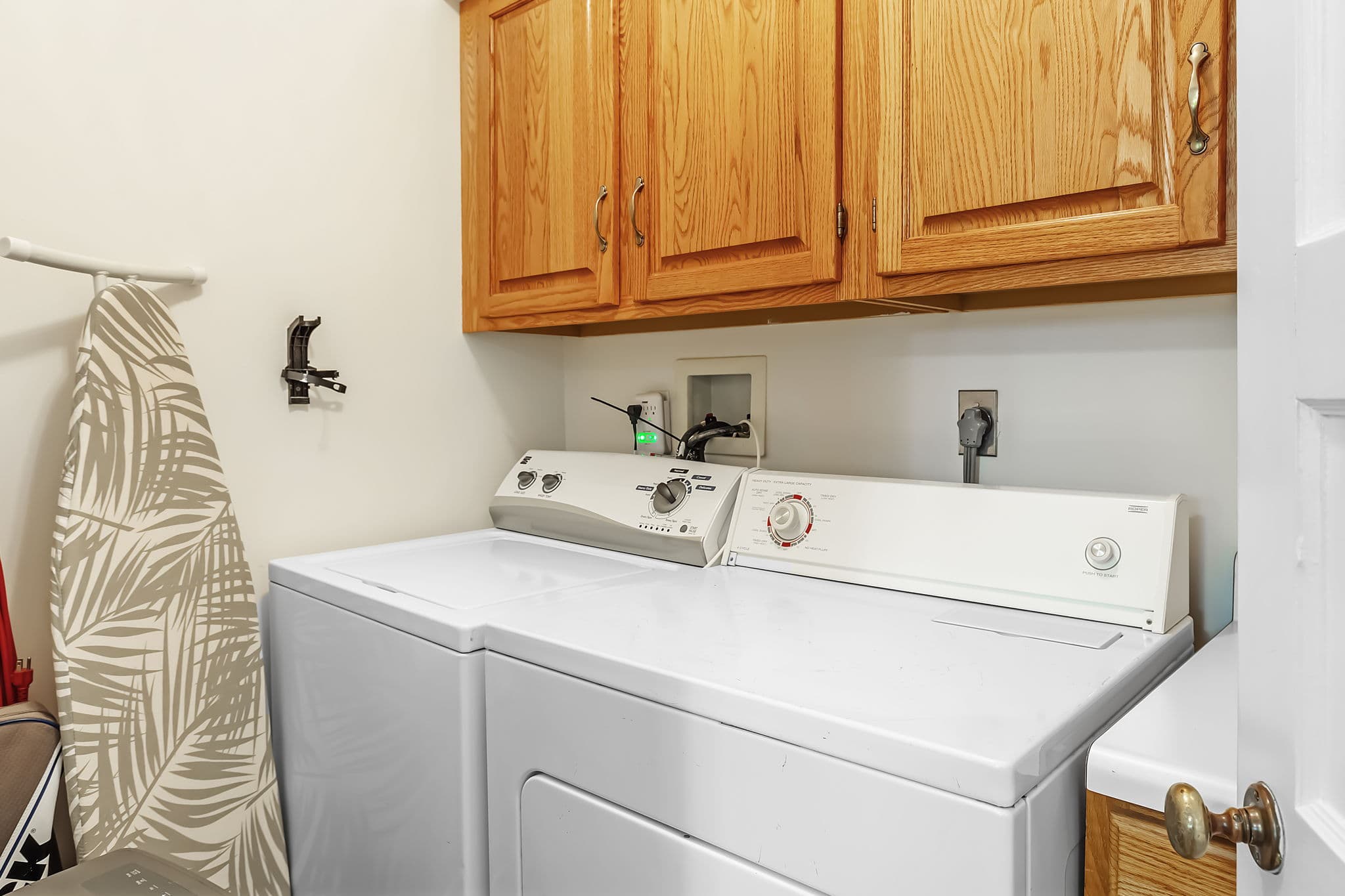A laundry room with a washer and dryer,, ironing board, and wood cabinets.