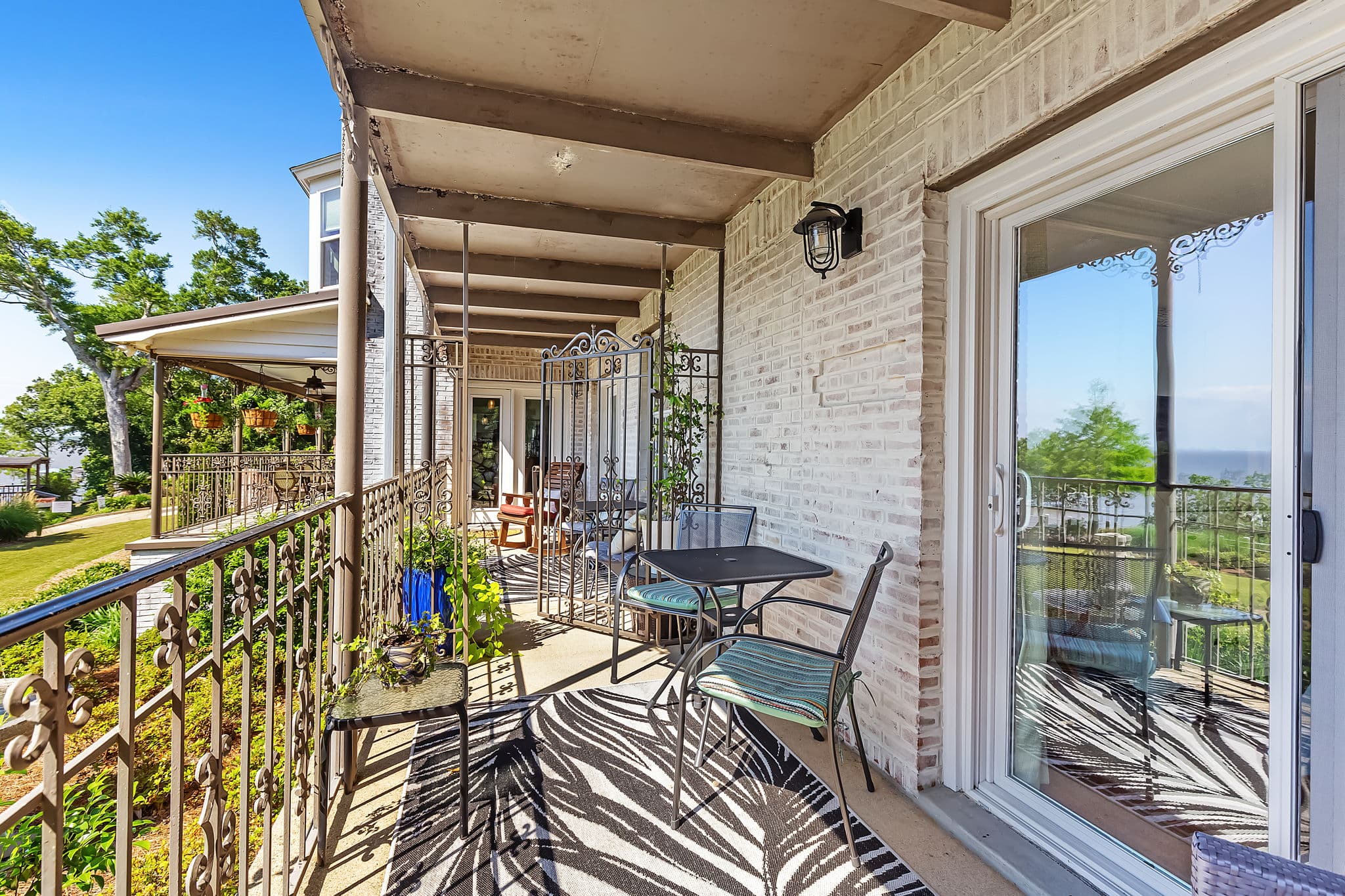 The Magnolia Porch Entrance to Bay View Room features a spacious balcony with a wrought iron railing, and there's a small table and chairs set up for outdoor dining. The balcony is covered by a roof for shade.