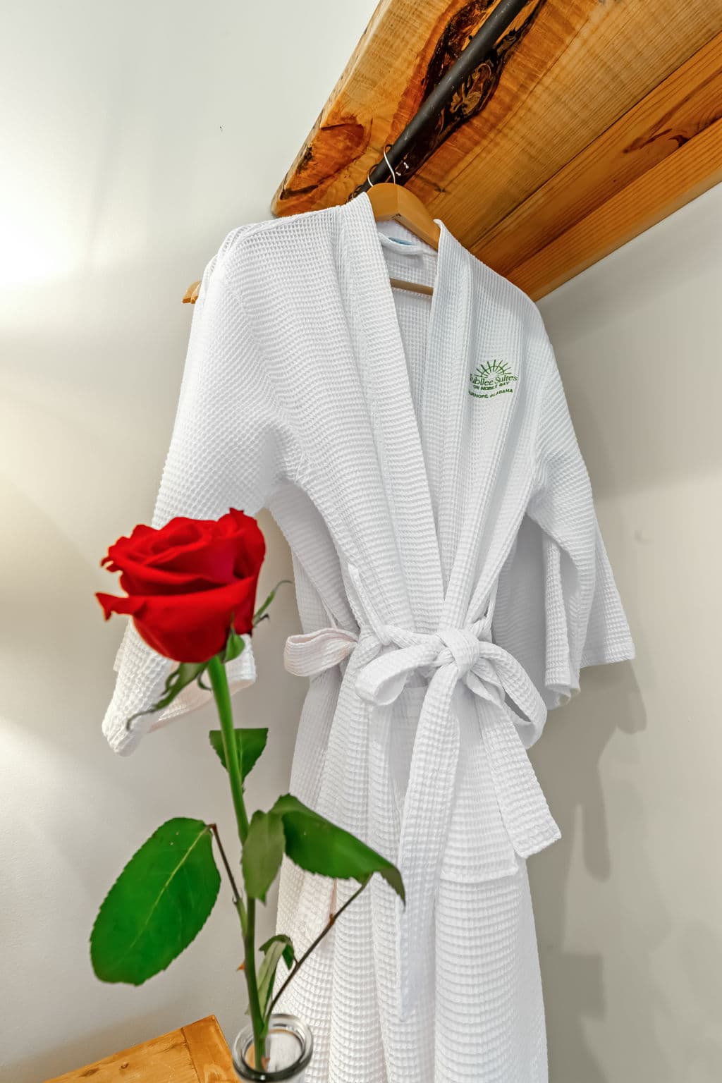 A white bathrobe hangs on a hook, and next to it, a single red rose adds a touch of elegance.