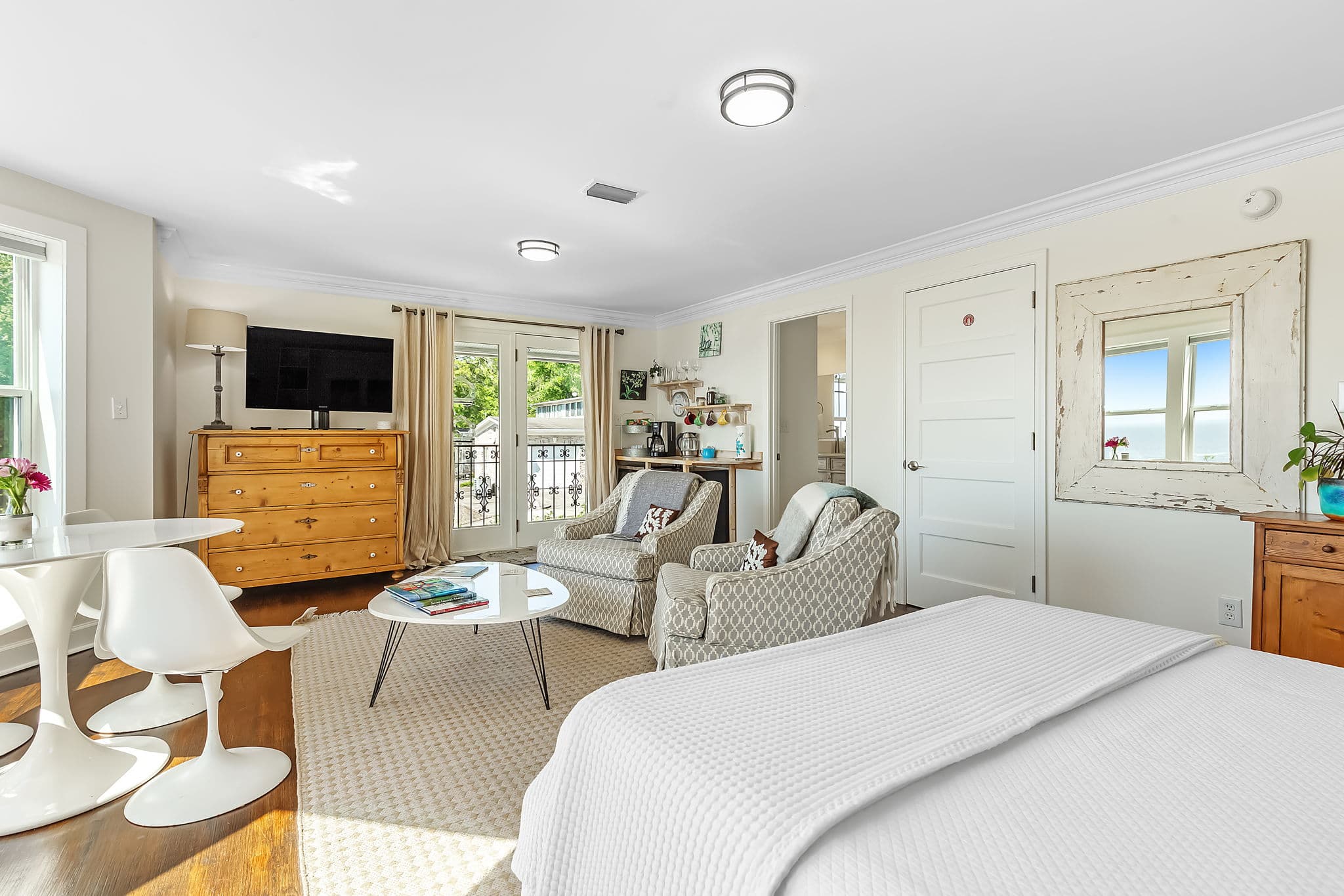 A spacious bedroom with large windows, a comfortable bed, seating area, and a small dining table.