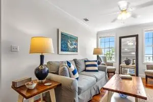 A cozy living room with a blue and white couch, wooden coffee table, and bright windows.
