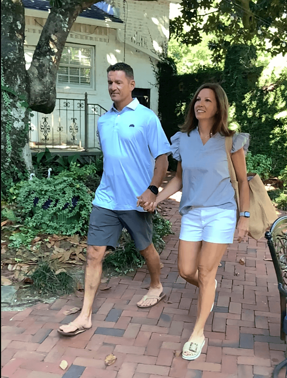A couple strolls hand-in-hand along a brick pathway surrounded by greenery.