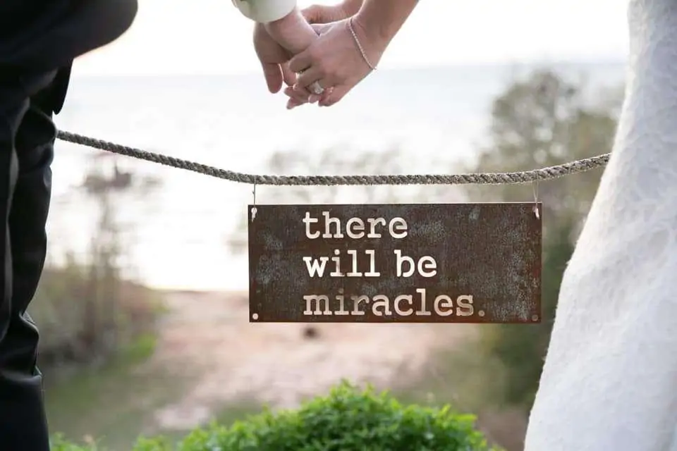 A couple holds hands in front of a sign that reads, "there will be miracles."
