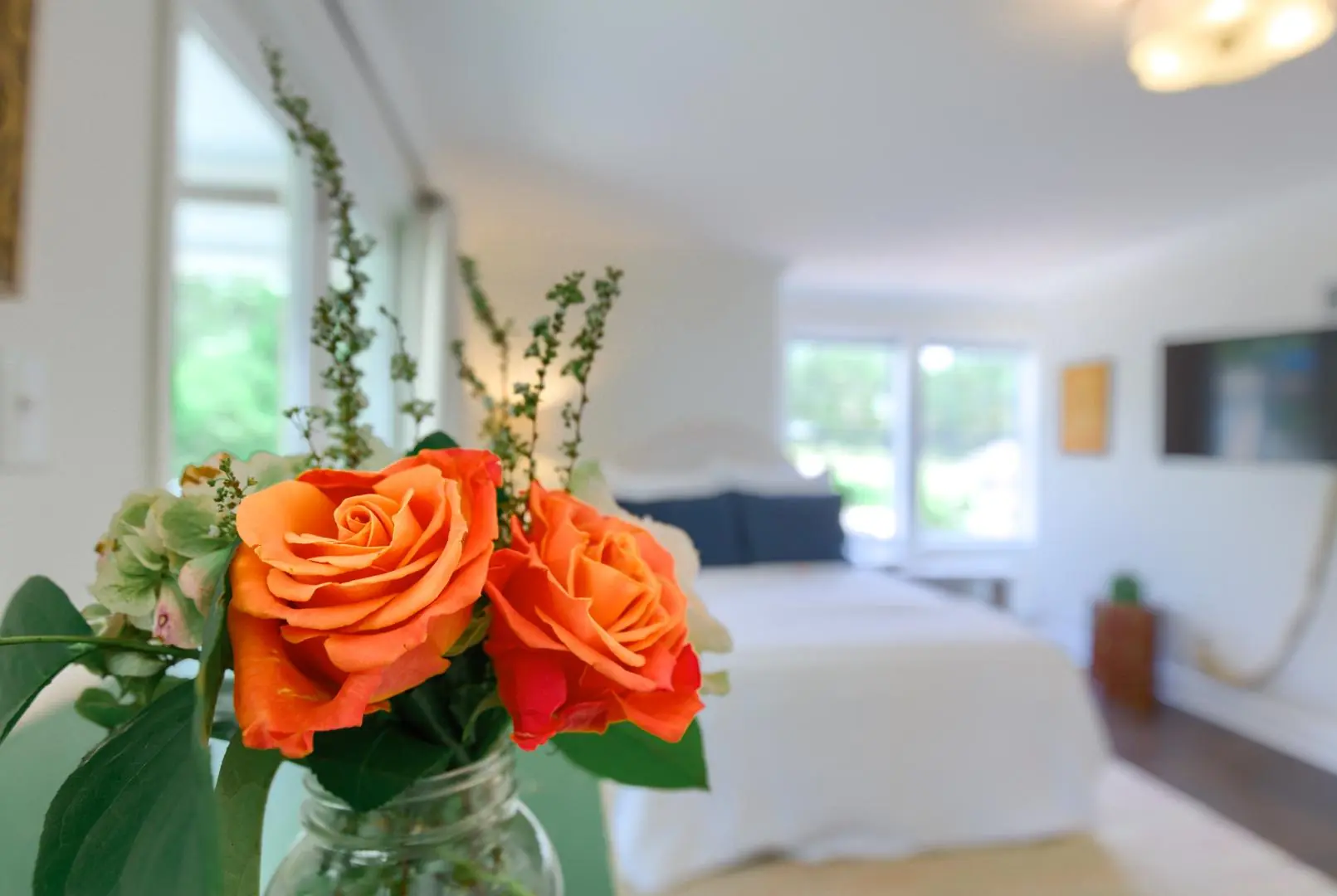 A close-up of orange roses in a jar, with a softly lit bedroom in the background. A close-up of orange roses in a jar, with a softly lit bedroom in the background.