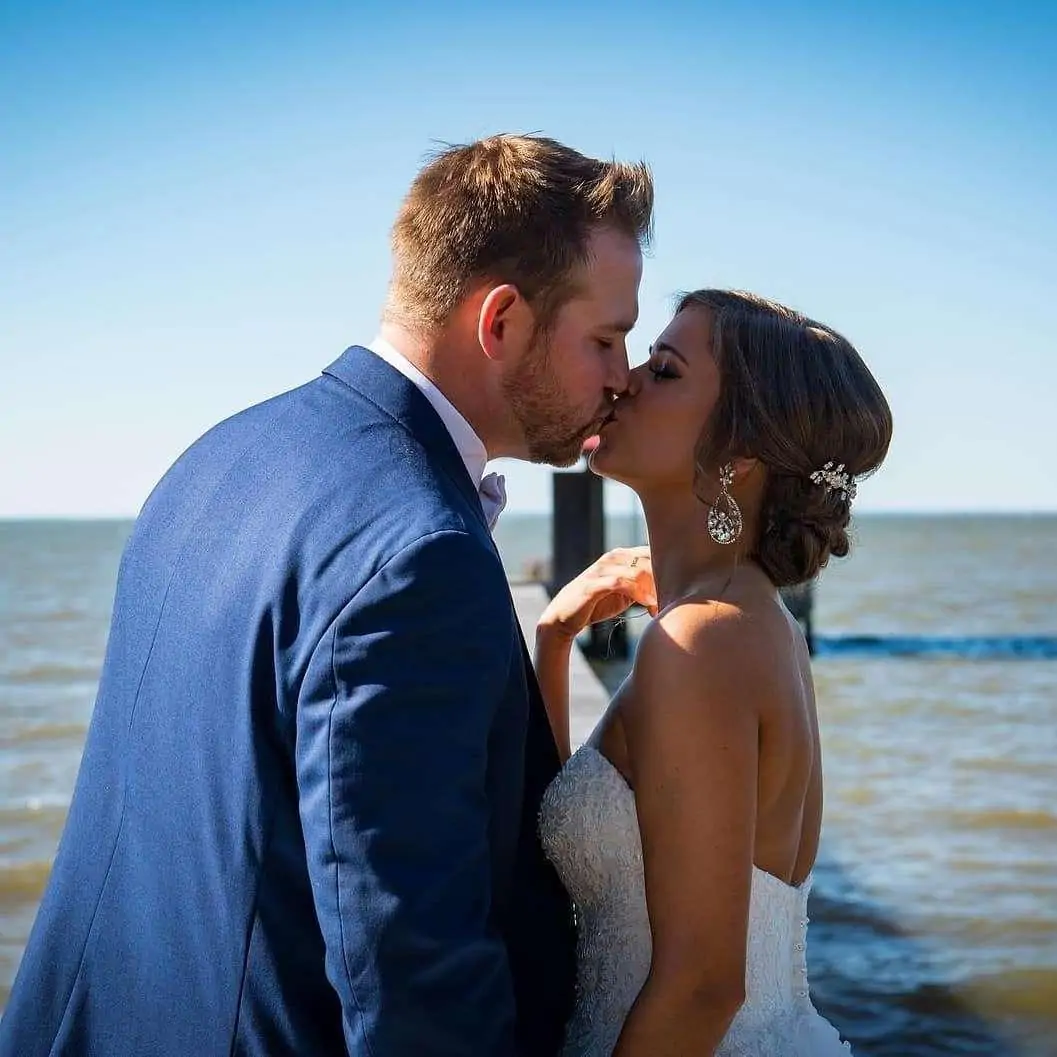 A couple kisses by the water on a sunny day.