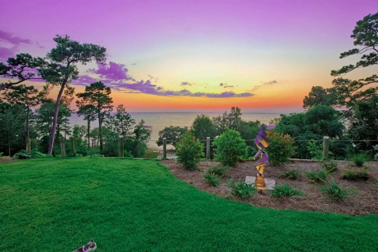 A vibrant sunset over a serene beach, framed by lush greenery and a colorful sculpture.