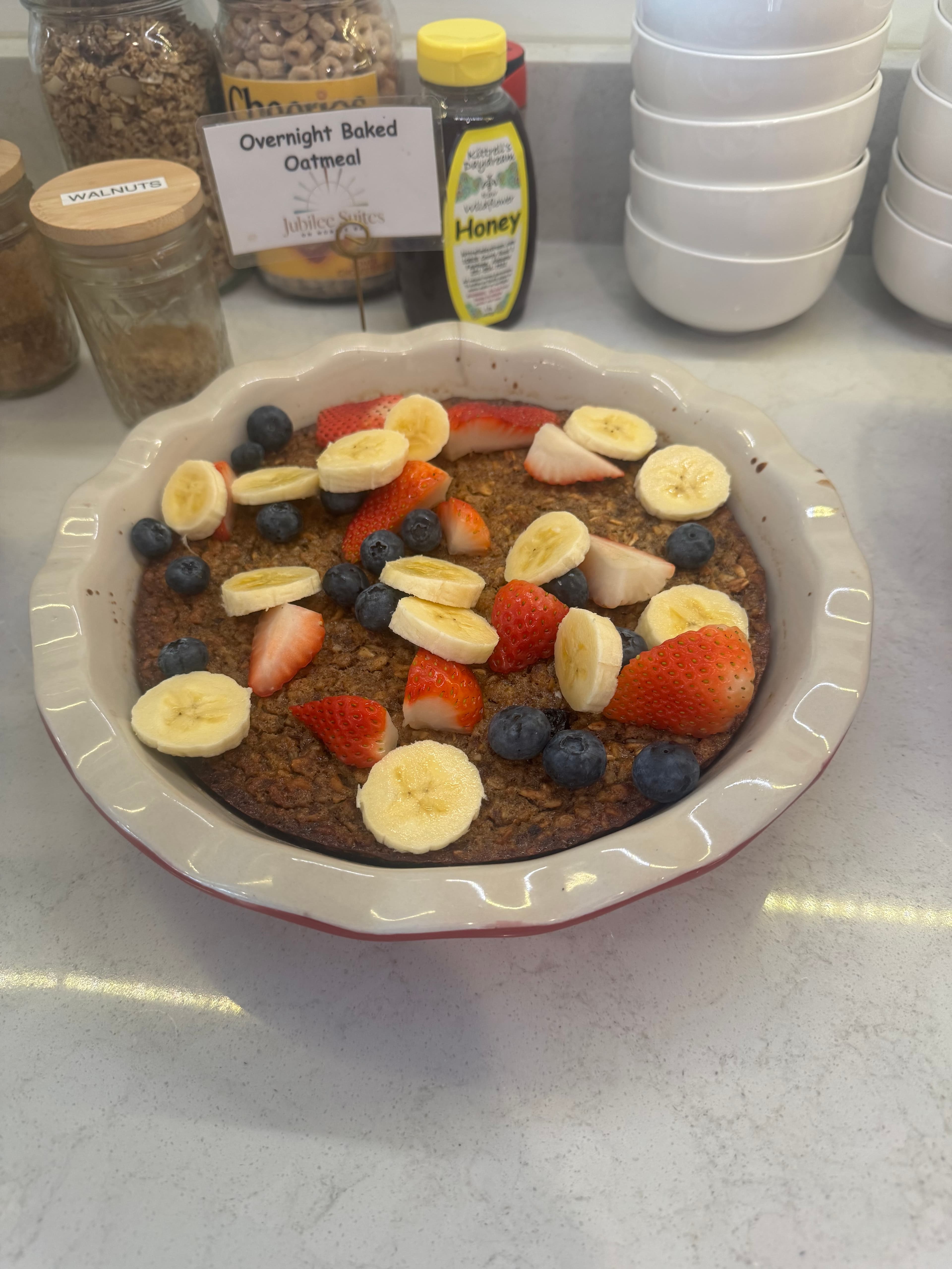 A dish of overnight baked oatmeal topped with sliced bananas, strawberries, and blueberries, set on a countertop. A dish of overnight baked oatmeal topped with sliced bananas, strawberries, and blueberries, set on a countertop.