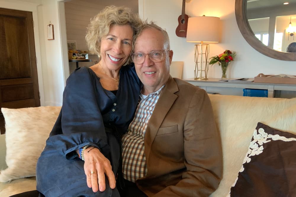 A middle aged man and woman sitting close to each other on a couch smiling for a picture