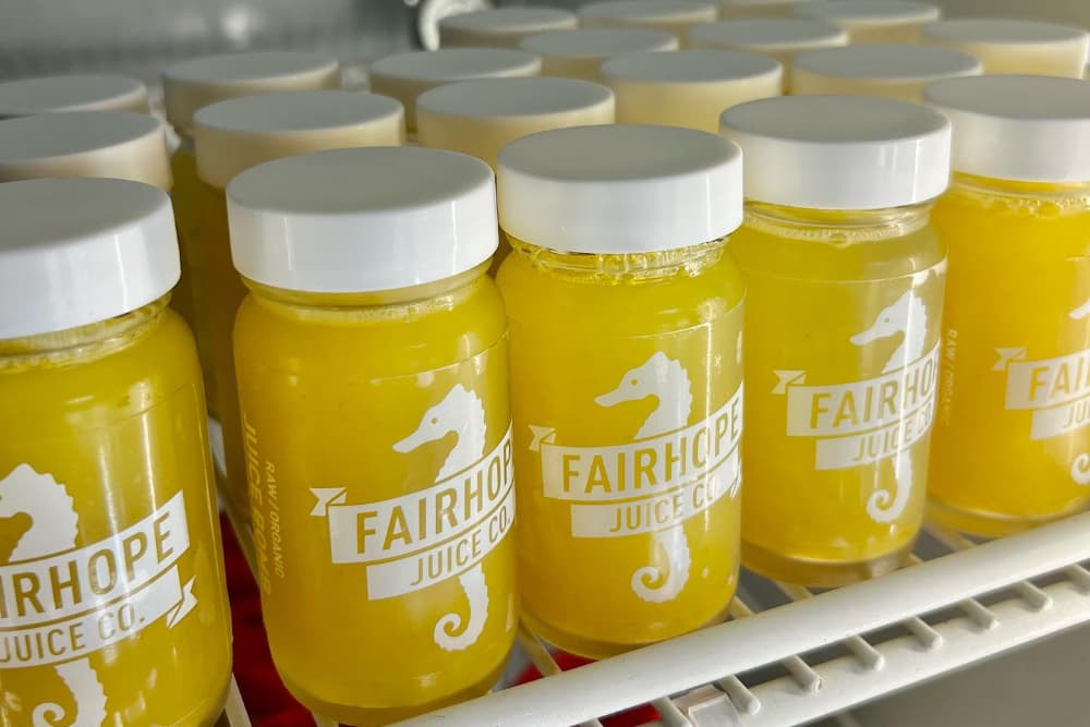 A refrigerator shelf stocked with lots of bottles of fresh orange juice labeled Fairhope Juice Company with a seahorse emblem.