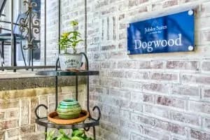 A blue sign labeled "Dogwood" is mounted on a brick wall next to a tiered plant stand with potted plants.
