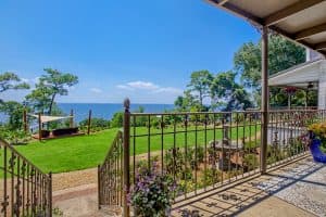 View from a terrace overlooking a lush green garden and a serene body of water under a clear blue sky.