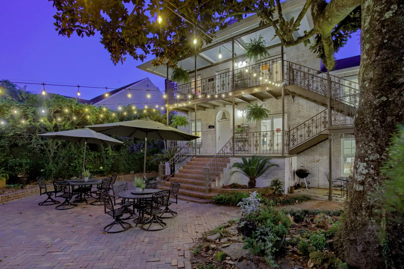 A beautifully lit outdoor patio with tables, umbrellas, and a two-story house in the background.