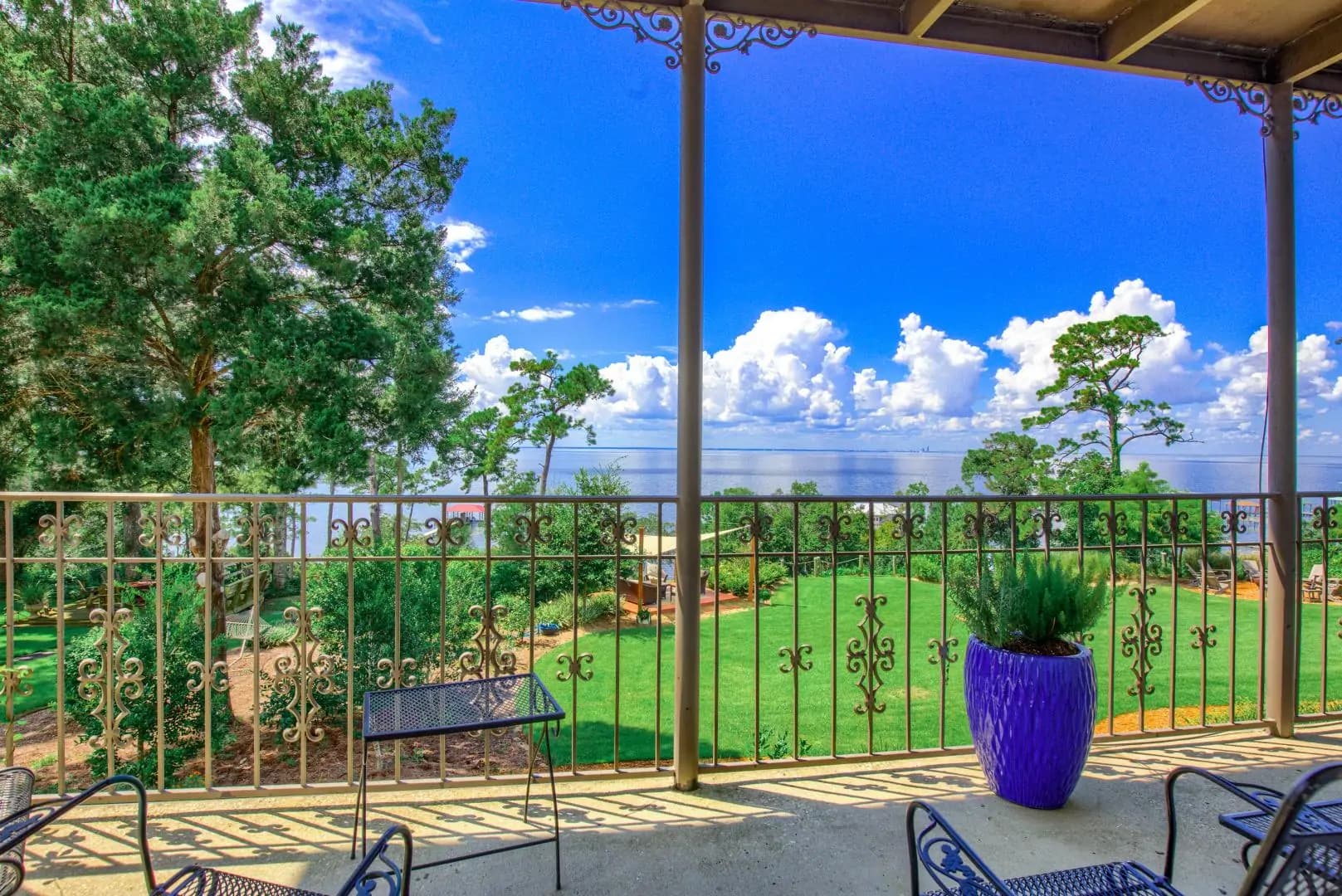View from a balcony overlooking a lush green lawn and lake under a blue sky with fluffy clouds. View from a balcony overlooking a lush green lawn and lake under a blue sky with fluffy clouds.