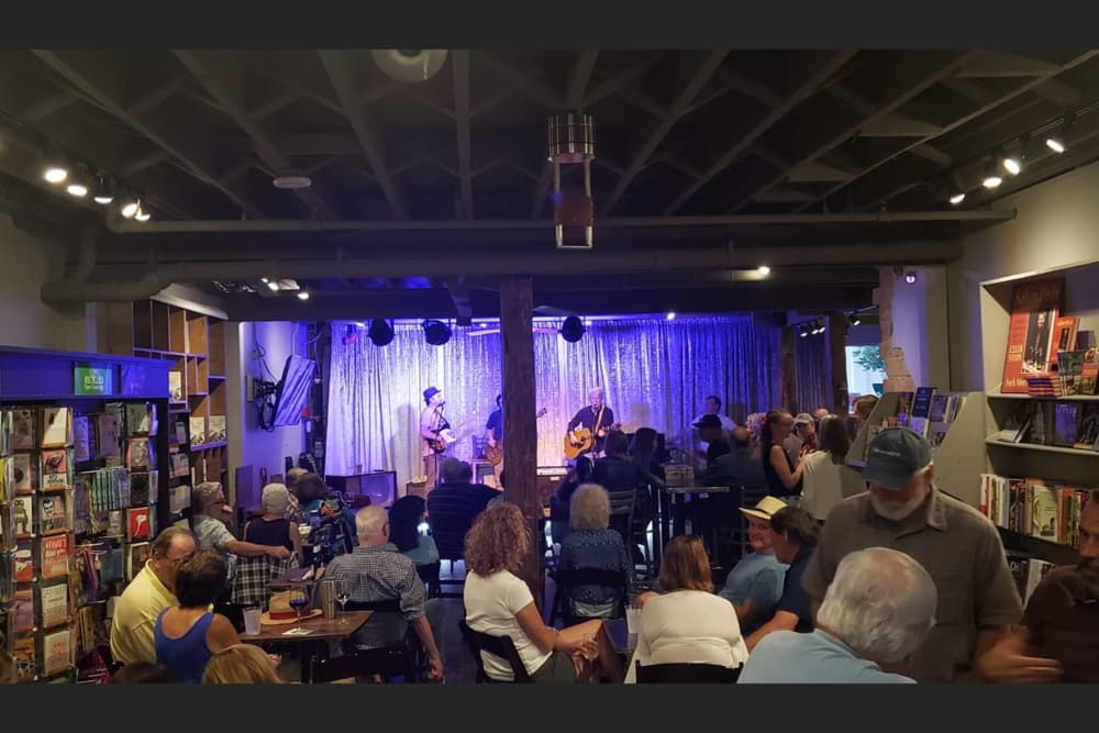 A bookstore setup with tables and chairs and a stage and a band performing music.