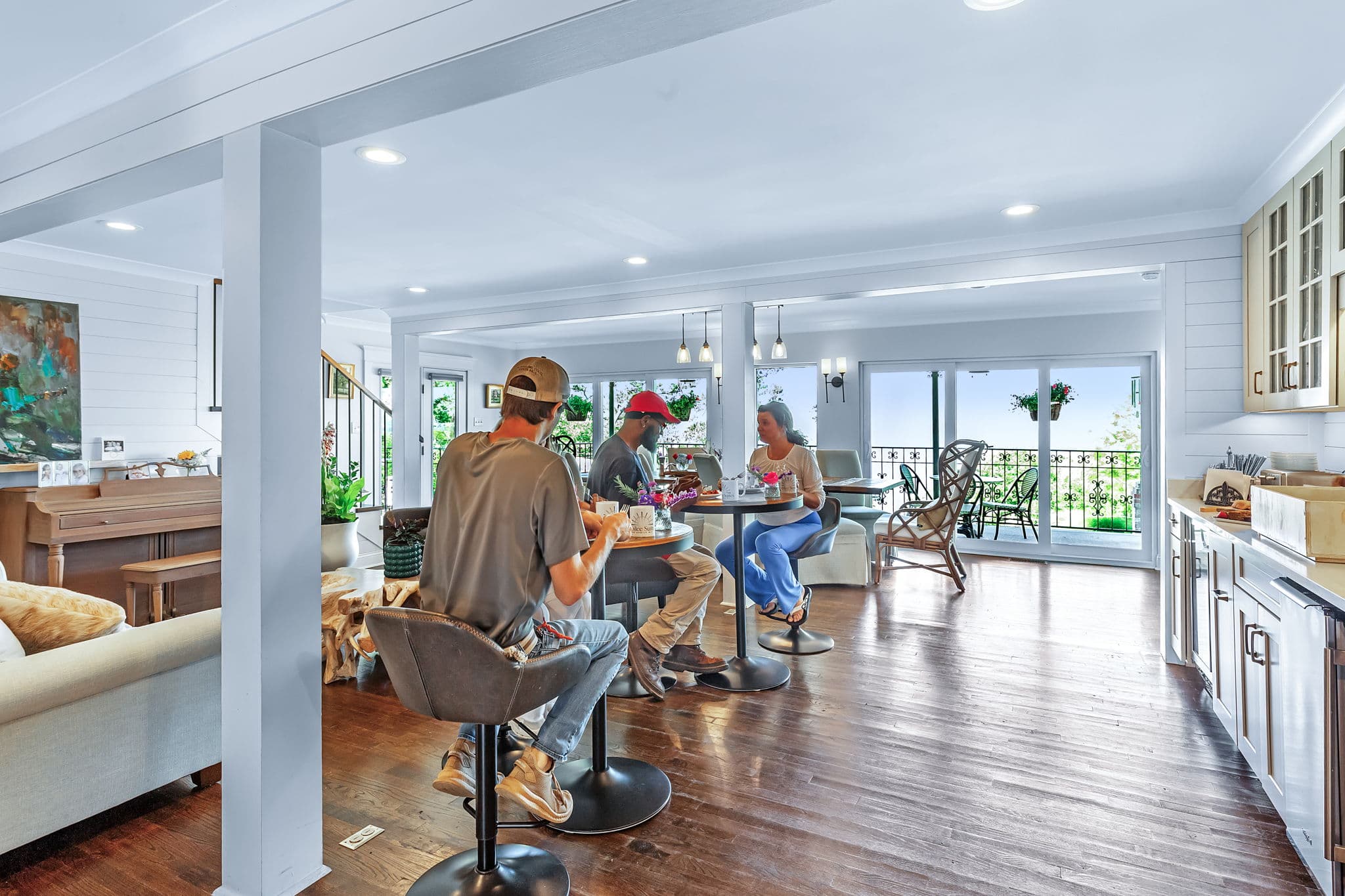 A group of people enjoying breakfast at tables for two in a spacious living and dining area, with sliding doors out to a terrace and views of Mobile Bay.