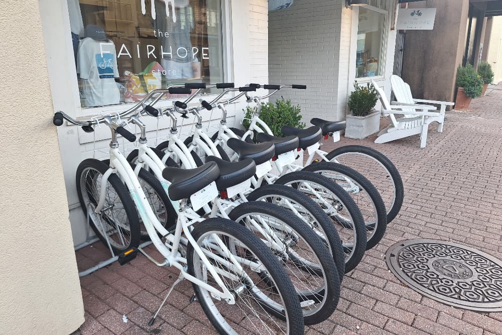Several white and black bicycles standing up and waiting for riders in front of The Fairhope Store