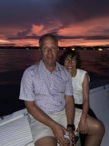 A man and a woman sit together on a boat against a sunset background.