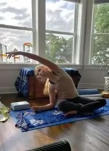 A person performs a yoga stretch on a mat in a sunlit indoor space.