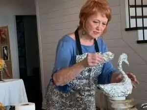 A woman in an apron artfully shapes a swan figure out of foil.