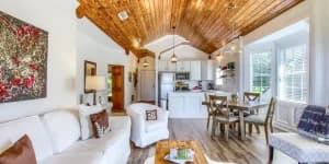 Cozy living area with high wooden ceilings, light-colored furniture, and a dining table.
