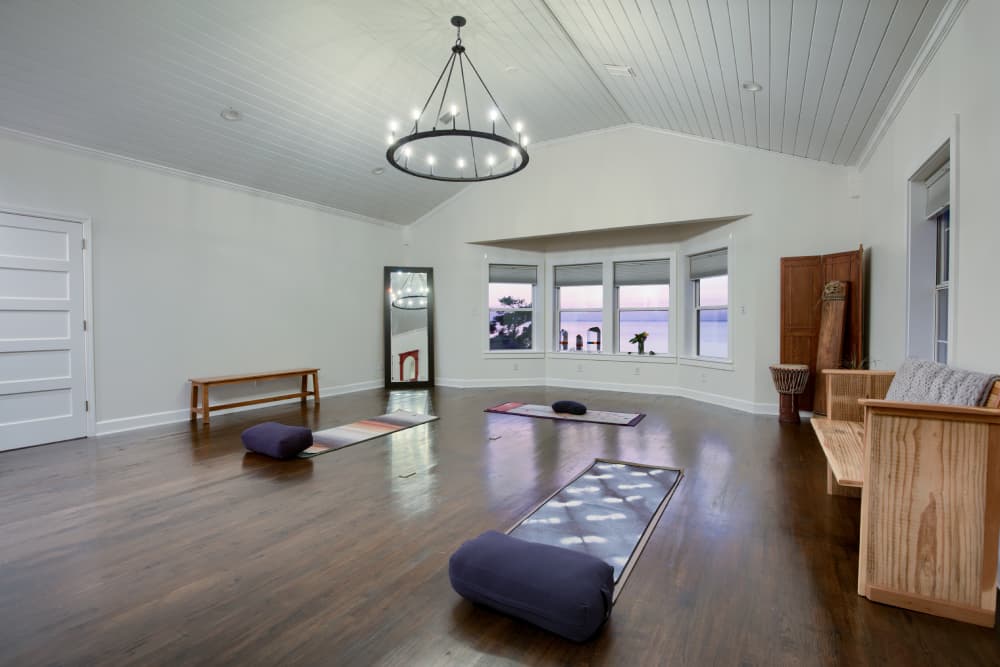 Yoga studio with vaulted ceilings and hard wood floors, windows look out to bay.
