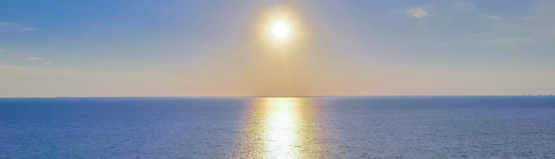 A bright sun shines over a calm ocean reflecting its light.