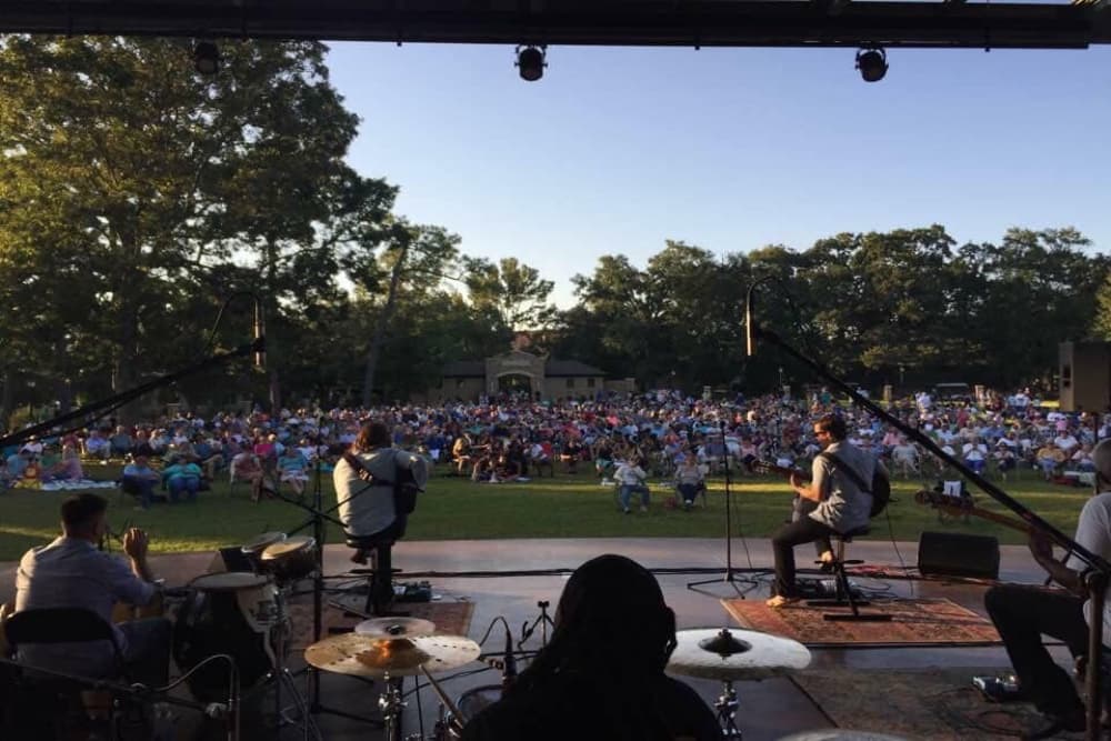 A group of people at an outdoor concert with people sitting on the grass watching a band perform on stage.