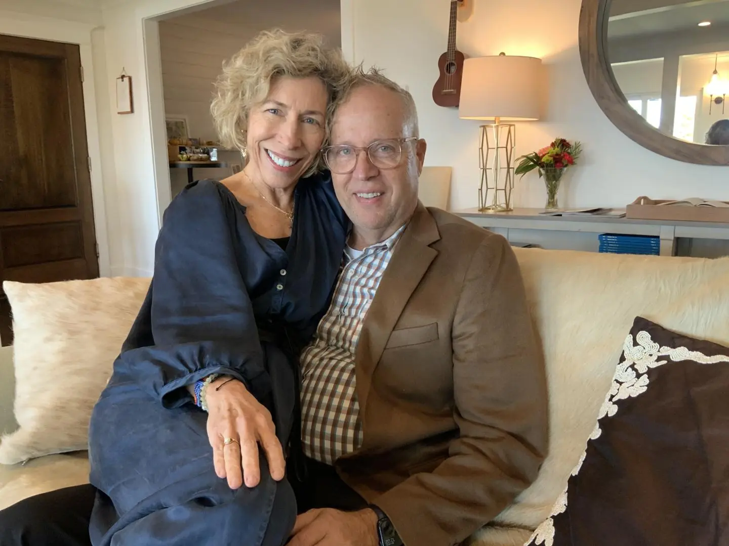 A smiling couple sits closely together on a couch in a cozy living room.