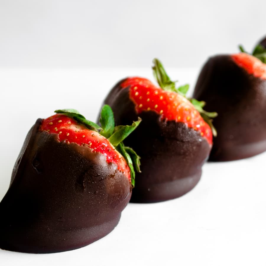 A white plate with 3 ripe red strawberries dipped in rich dark chocolate