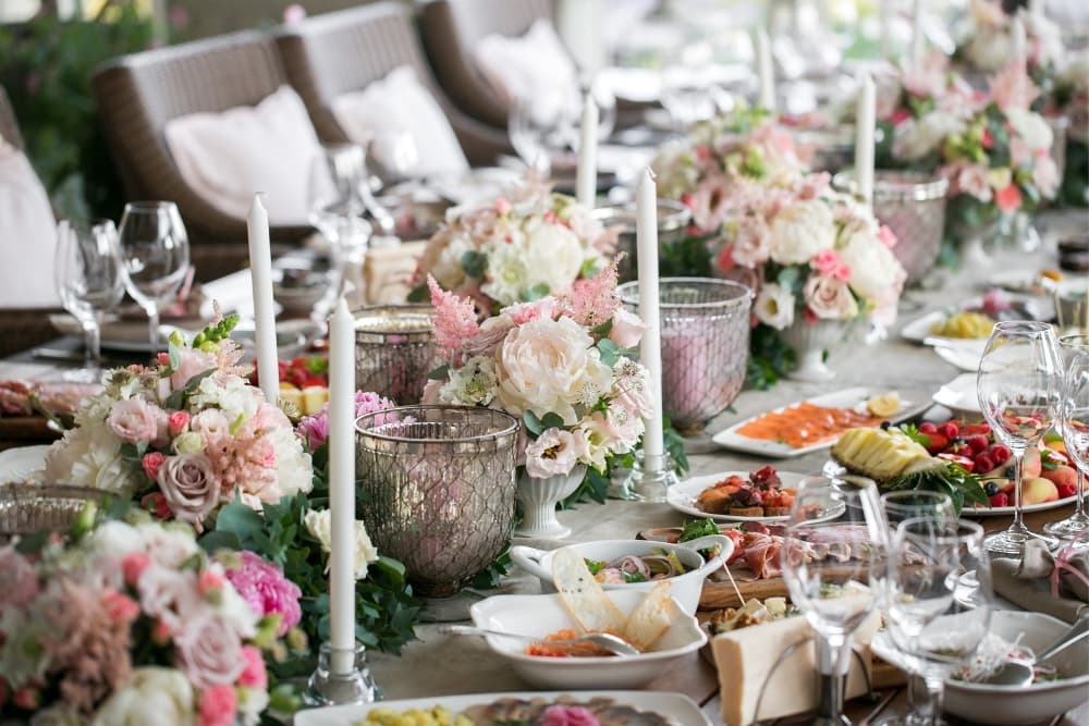 A table overflowing with delicious food, including charcuterie, seafood, and fruit, alongside stunning floral arrangements.