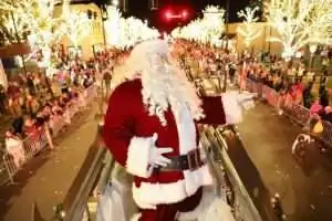 A festive Santa Claus waves to a crowd during a illuminated holiday parade.