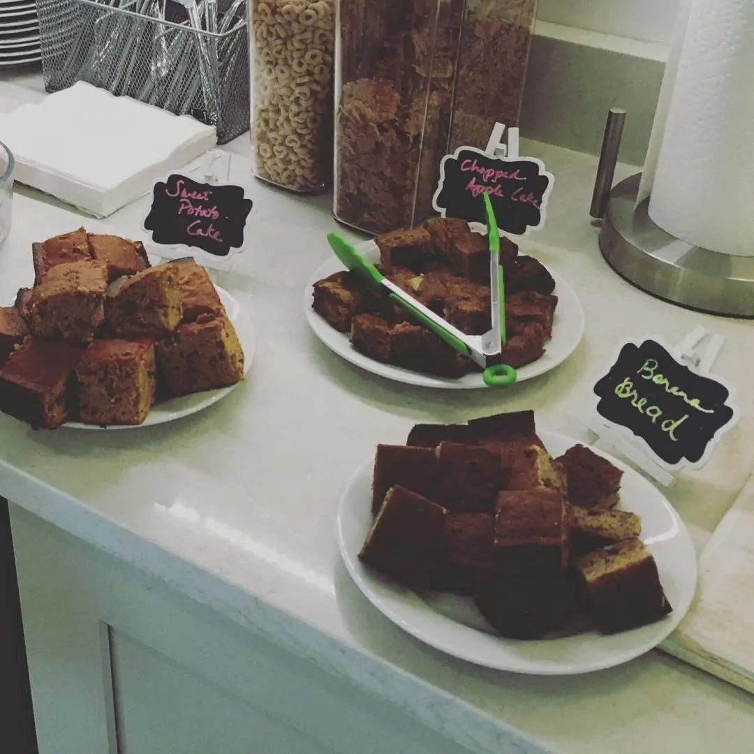 Three plates of baked goods, labeled as sweet potato cake, chopped apple cake, and banana bread, are arranged on a countertop. Three plates of baked goods, labeled as sweet potato cake, chopped apple cake, and banana bread, are arranged on a countertop.