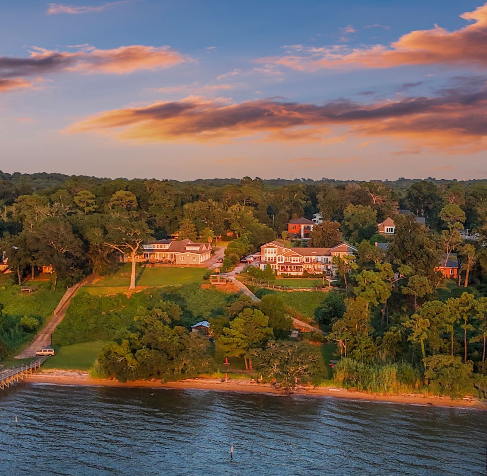 Aerial view of lakeside homes surrounded by greenery at sunset.
