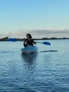 A person kayaks on calm blue water against a clear sky.